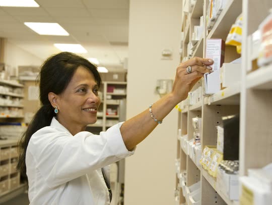 A pharmacist reaches for a box of medicine on a dispensary shelf